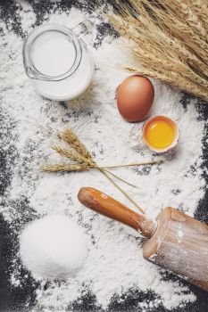 Bake dough recipe ingredients eggs, flour, milk, butter, sugar and rolling pin on dark background. Background with free text space