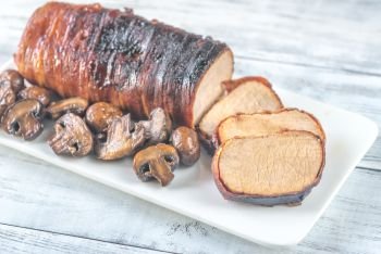 Pork loin wrapped in bacon with roasted mushrooms