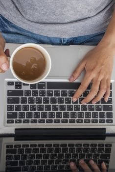 Woman’s left hand on the keyboard and right hand holding a cup of coffee