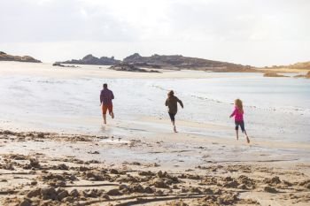 happy dad and two daughters running along the beach at low tide. typical Brittany coast at  the Tregastel in the north of France
