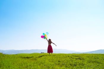 Happy girl in the meadows tuscan with colorful balloons, against the blue sky and green meadow. Tuscany, Italy
