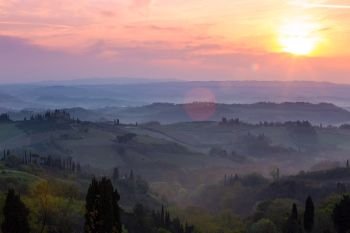 fog and typical Tuscan landscape - a view of a villa on a hill, a cypress alley and a valley with vineyards, province of Siena. Tuscany, Italy
