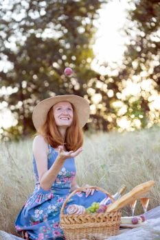 Summer - Provencal picnic in the meadow. Fun smiling girl sitting near a picnic basket and baguette, wine, glasses, grapes and rolls
