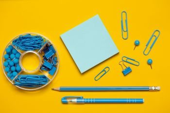 stationery paper clips, binders, buttons, pencil, pen and paper in blue on yellow background
