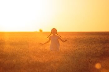little girl running at the orange evening wheat field 

