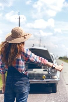 young woman hitch-hiking on a road at the fields
