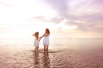 happy fun weekend by the sea - Mom and daughter in white dresses whirling by the sea at sunset. Ukrainian landscape at the Sea of Azov, Ukraine
