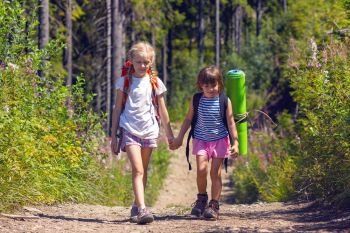 little children on a hike. Fun girl girlfriends go along the trail against the backdrop of a pine forest
