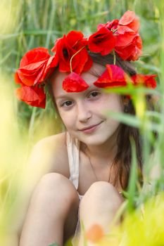 close up portrait of child girl with circlet of poppies sitting at the grass
