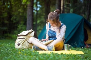 girl hiker reading a book near the tent
