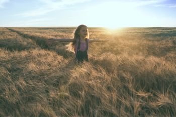 little girl running at the orange evening wheat field 
