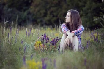 summer. Girl teenager sitting alone in a meadow. Near the basket with sage
