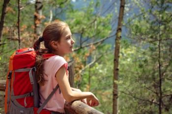 girl with backpack standing on a forest trail
