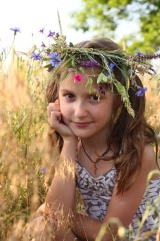 girl with flowers diadem on her head posing at the field.