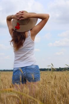 young girl joys on the wheat field with blue cloudy sky at the background.