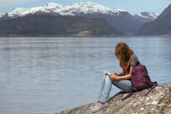 girl hiker with a book sitting on a rock on a background of mountains and lakes, norway
