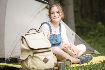 smiling girl hiker sitting and reading a book near the tent
