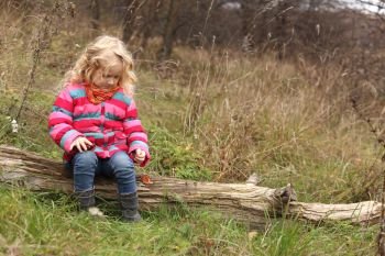 child girl sitting on a log at the autumn forest
