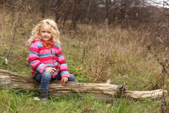child girl sitting on a log at the autumn forest
