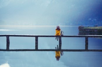 girl tourist in a hat and with a backpack stands on a wooden bridge on a mountain lake in the early morning. beautiful landscape and reflection
