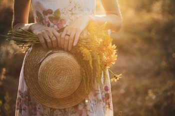 girl in a field at sunset with a hat and a bouquet of wildflowers
