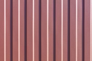 Brown metallic fence made of corrugated steel sheet with vertical guides. Corrugated brown iron sheet background close up.. Brown corrugated steel sheet with vertical guides.