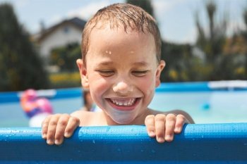 Portrait of happy smiling boy playing in a pool having fun on a summer sunny day. Close up of smiling kid looking at camera. Happy boy playing in a pool