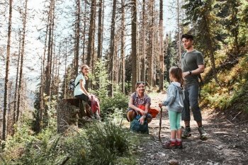 Family with backpacks hiking in a mountains actively spending summer vacation together walking on forest path talking and admiring nature mountain landscapes. Family with backpacks hiking in a mountains actively spending summer vacation together