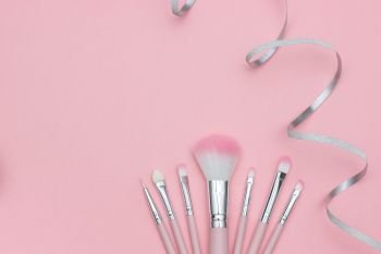 Set of makeup brushes and silver ribbon serpentine on pastel pink background.. Set of makeup brushes and silver ribbon serpentine on pastel pink background