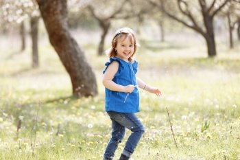 A beautiful cute little girl laughs and has fun in a blue blouse with a chamomile flower in a spring garden. A beautiful cute little girl laughs and has fun in a blue blouse with a chamomile flower in a spring garden.