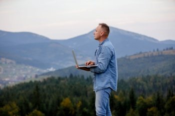Man working outdoors with laptop in mountains. Concept of remote work or freelancer lifestyle. Cellular network broadband coverage. internet 5G. Man working outdoors with laptop in mountains. Concept of remote work or freelancer lifestyle. Cellular network broadband coverage. internet 5G.