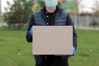 Delivery man in face medical mask, gloves hold empty cardboard box outdoors. Service coronavirus. Online shopping. mock up. Delivery man in face medical mask, gloves hold empty cardboard box outdoors. Service coronavirus. Online shopping. mock up.