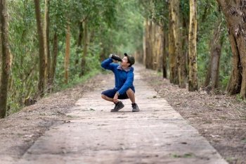 Asian runner in sport suit are running with happiness action drinking the water from sport bottle with relax action in deep forest in evening time, lifestyle and leisure concept