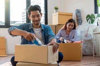 Asian young couple packing big cardboard box for moving in new home, Moving and House Hunting concept
