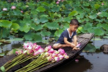 Vietnamese boy playing with pink lotus leaf when his mom boating the traditional wooden boat in the big lake at thap muoi, dong thap province, vietnam, culture and life concept