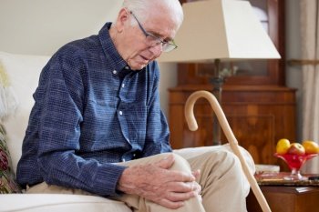 Senior Man Sitting On Sofa At Home Suffering With Knee Pain From Arthritis