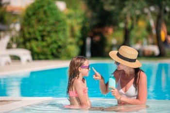 Young mother applying sun cream to daughter nose on the beach vacation. The concept of protection from ultraviolet radiation. Young mother applying sun cream to daughter nose on the beach.