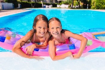 Little kids in pool swimming on air matress on summer vacation. Adorable little sisters play in outdoor swimming pool