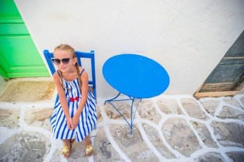 Cute girl in dress at street of typical greek traditional village with white walls and colorful doors on Mykonos Island, in Greece. Girl in blue dresses having fun outdoors on Mykonos streets