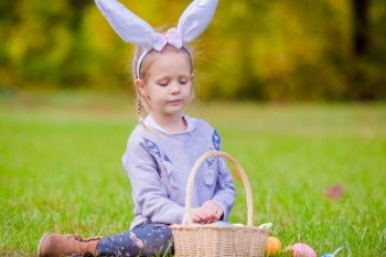 Adorable girl wearing bunny ears holding basket with Easter eggs. Adorable little girl wearing bunny ears with a basket full of Easter eggs on spring day outdoors