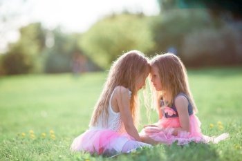 Adorable little girls on beautiful spring day outdoors having fun together. Adorable little girls on spring day outdoors sitting on the grass