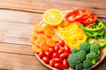 Top view of fresh organic fruits and vegetables in plate wood (carrot, Broccoli, tomato, orange, Bell pepper) on wooden table, Healthy lifestyle diet food concept