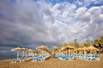 Sun loungers in the morning on a sandy beach by the Mediterranean Sea at the popular resort of Marbella, Costa del Sol, Andalusia, Spain.