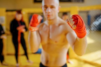 Male MMA fighter with red bandages on his hands in gym. Muscular man on ring, combat workout, martial arts training. Male MMA fighter with red bandages on his hands