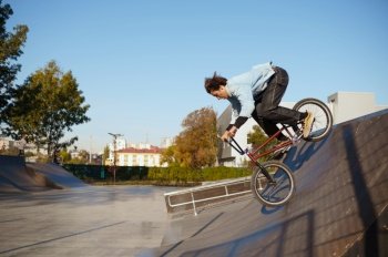 Bmx biker doing trick on ramp,teenager on training in skatepark. Extreme bicycle sport, dangerous cycle exercise, risk street riding, biking in summer park. Bmx biker doing trick on ramp in skatepark
