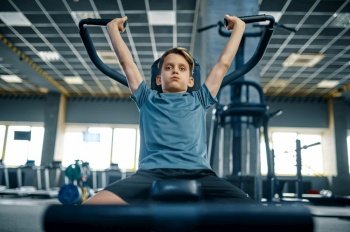 Boy on exercise machine, front view, training in gym. Youngster in sport club, healthcare and healthy lifestyle, schoolboy on workout, sportive youth. Boy on exercise machine, front view