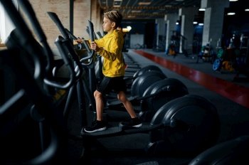 Child on exercise machine, side view, training in gym. Youngster in sport club, healthcare and healthy lifestyle, schoolboy on workout, sportive youth. Child on exercise machine, training in gym
