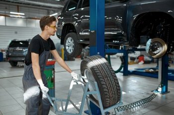 Male mechanic fixes problem with wheel, car service. Vehicle repairing garage, man in uniform, automobile station interior on background. Mechanic fixes problem with wheel, car service
