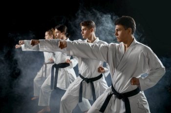Four karate fighters poses in white kimono, group training, dark smoky background. Karatekas on workout, martial arts. Four karate fighters poses in white kimono