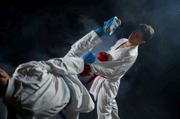 Two male karatekas in white kimono and gloves, combat in action, dark background. Fighters on workout, martial arts, fighting competition. Two male karatekas in white kimono and gloves